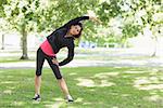 Full length portrait of a healthy young woman doing stretching exercise in the park