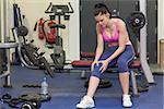 Full length of a healthy young woman with an injured knee sitting in the gym