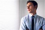 Elegant young businessman peeking through blinds in office