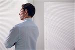 Rear view of a young businessman peeking through blinds in office