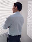 Rear view of a young businessman peeking through blinds in office