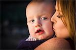 Adorable Red Head Infant Boy is Kissed By His Mother Outdoors in Dramatic Lighting.