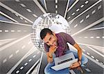 Composite image of thoughtful man sitting on floor using laptop and smiling at camera