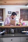 Man and baby sitting at kitchen counter looking at digital tablet