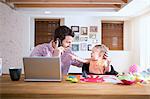 Man and baby sitting at kitchen counter making phone call