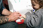 Father painting heart shape on daughter's hand