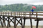 Teenage girl running with umbrella on pier, Bainbridge Island, Washington, USA