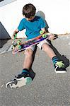 Teenage boy sitting on ground preparing skateboard