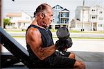 Portrait of muscular senior man lifting dumb bells