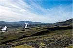 View of the Nesjavellir Geothermal Power Station with white smoke, blue sky, clouds streaked moss green and mountains, Nesjavellir, Iceland, Europe