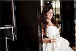 Portrait of bride in wedding gown, standing in doorway, holding glass of champagne, looking at camera and smiling, Ontario, Canada