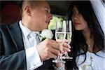 Close-up of Bride and Groom in car, looking at each other and toasting with champagne glasses on wedding day, Ontario, Canada