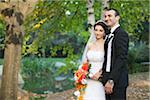 Portrait of bride and groom standing outdoors next to trees in public garden, in Autumn, Ontario, Canada