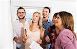 Mature businesswoman meeting with group of young business people, looking at white board and smiling, Germany