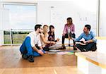 Mature businesswoman meeting with group of young business people, sitting on floor in discussion, Germany