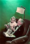 1940s 1950s GRANDDAUGHTER SITTING ON SMILING GRANDFATHER'S LAP READING PICTURE BOOKS