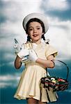 1950s SMILING GIRL WEARING YELLOW DRESS STRAW HAT HOLDING TOY RABBIT AND EASTER BASKET LOOKING AT CAMERA