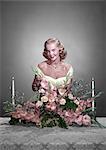 1950s SMILING WOMAN WEARING FORMAL GOWN ARRANGING FLOWERS CENTERPIECE ON DINING TABLE