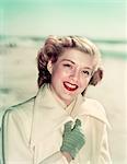 1940s 1950s PORTRAIT SMILING BLOND WOMAN WEARING WHITE OVERCOAT GLOVES OUTDOORS AT BEACH