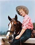 1940s 1950s SMILING BLOND TEEN GIRL WEARING WESTERN COWGIRL OUTFIT SITTING ON FENCE POSING BY HORSE LOOKING AT CAMERA