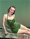 1940s PORTRAIT SMILING WOMAN WEARING GREEN VELVET BATHING SUIT SITTING POSING ON DIVING BOARD