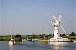 Sailing boats and river cruisers pass windmill on Norfolk Broads, United Kingdom