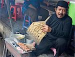 Muslim man in the market cooking chicken satay, fanning the charcoal with a palm leaf fan, Solo, Java, Indonesia, Southeast Asia, Asia