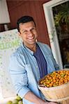 A farm growing and selling organic vegetables and fruit. A man holding a bowl of basket of freshly picked tomatoes.