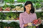 A farm stand with rows of freshly picked vegetables for sale. A woman holding a bunch of carrots.