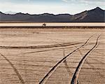 Tire tracks crisscrossing the surface on the Bonneville Salt Flats during speed week. A motorcyclist riding along a track.