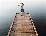 A ten year old girl playing the violin at dawn on a wooden dock.