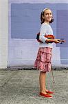 A ten year old girl holding a violin under her arm and a bow in her hand.