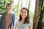 Two people, a young woman and man, walking side by side in the woods.