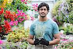 A young man working in a greenhouse full of flowering plants.