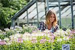 A woman in a plant nursery surrounded by flowering plants and green foliage.