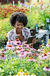 A woman in a plant nursery surrounded by flowering plants and green foliage.