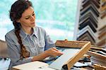 A woman in a picture framer's workshop, choosing frames and cardboard mounts. Surrounded by samples.