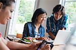 A group of three people in a cafe. Sharing a laptop and using smart phones.