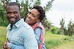 An organic apple tree orchard. A couple hugging and smiling at the camera.