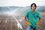 An organic vegetable farm, with water sprinklers irrigating the fields. A man in working clothes with his hands on his hips.