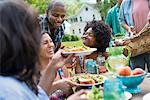 A group of adults and young people at a meal in the garden of a farmhouse. Passing plates and raising glasses.