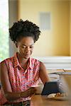 A woman seated having a cup of coffee. Holding an ebook or a digital tablet.