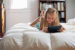 A young girl sitting on her bed using a digital tablet.