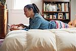 A young woman lying on her bed using a digital tablet.