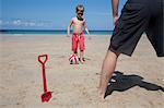 A boy playing football with a man on the sand. Father and son. A beach spade upright in the sand.