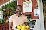 Working on an organic farm. A man carrying a large basket of yellow squash vegetables. Displays of fresh produce for sale.