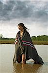 Young Women Wrapped in Blanket Standing in Large Puddle in the Country.