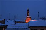 Night view on snowy roofs and illuminated church Madonna Moretta in Alba, northern Italy.