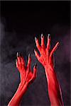 Red devil hands with black sharp nails, Halloween theme, studio shot over smoky background