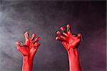 Spooky red devil hands with black glossy nails, Halloween theme, studio shot over smoky background